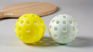 Side by side comparison of a yellow 40-hole rotomolded pickleball and a white 48-hole injection molded pickleball on a court background